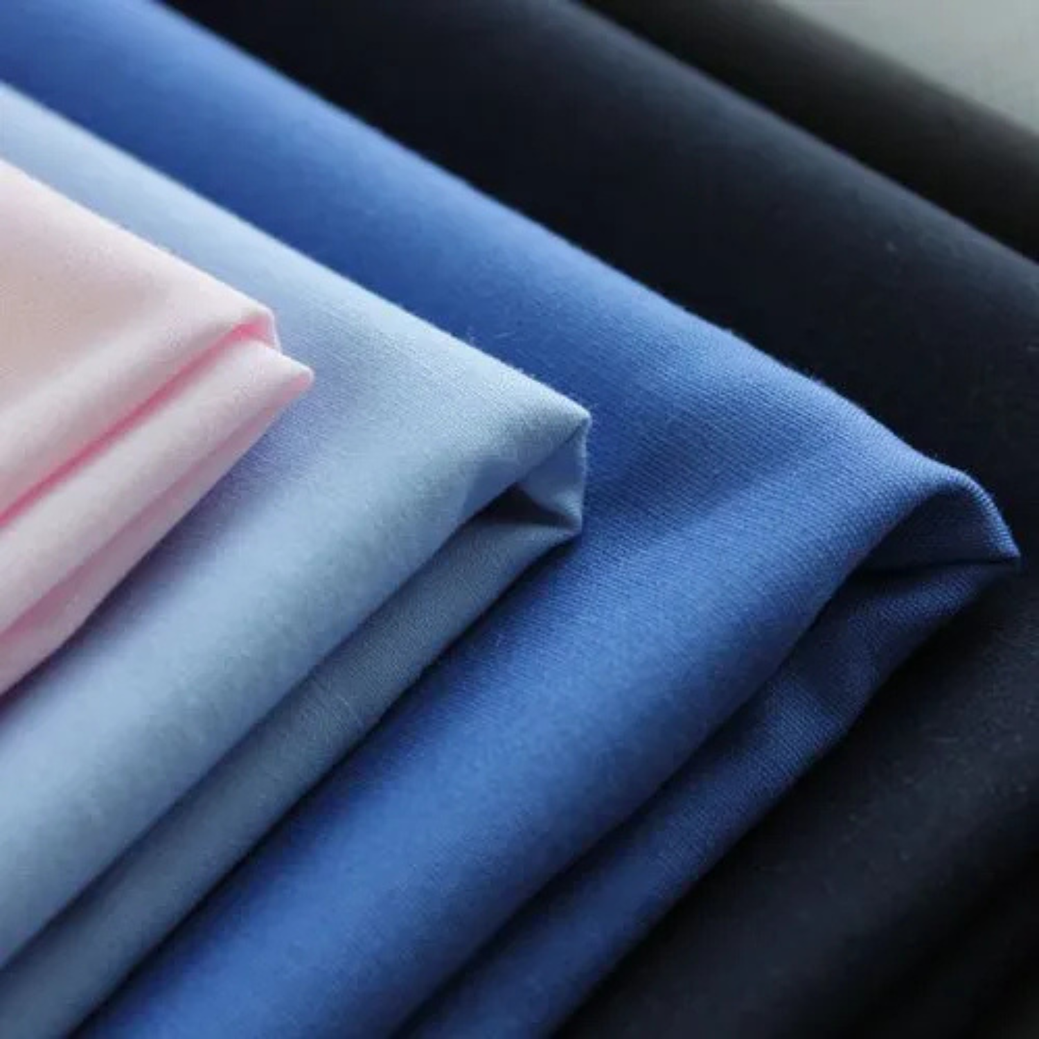 stack of folded smooth uniform fabric in shades of blue, pink, and navy for tailoring and garment manufacturing.
