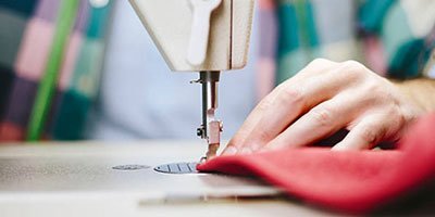 Tailor stitching fabric on sewing machine Imperial Clothes custom uniform manufacturing.