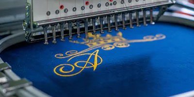 Embroidery machine stitching custom logo design on fabric Imperial Clothes.